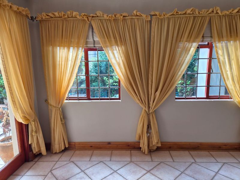 A bright living area featuring tiled flooring, timber window frames with security bars, and neutral wall finishes.