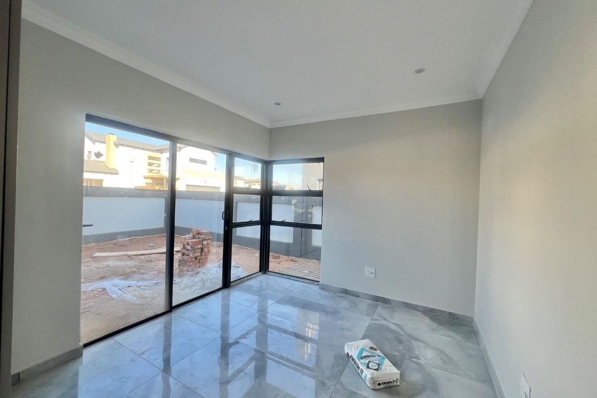 A bright, modern living area featuring large black-framed sliding glass doors that open onto an outdoor space, finished with polished grey floor tiles.