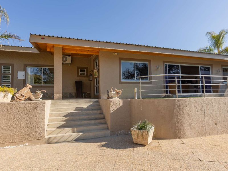 Front elevation of a single-story house featuring concrete stairs, a raised patio area with stainless steel balustrades, and paved driveway access.