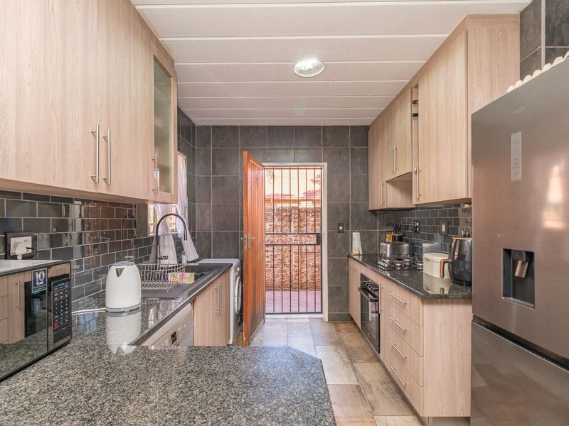 Modern kitchen featuring light wood cabinetry, granite countertops, dark tiled backsplash, built-in oven, and direct access to an exterior area via a security gate.