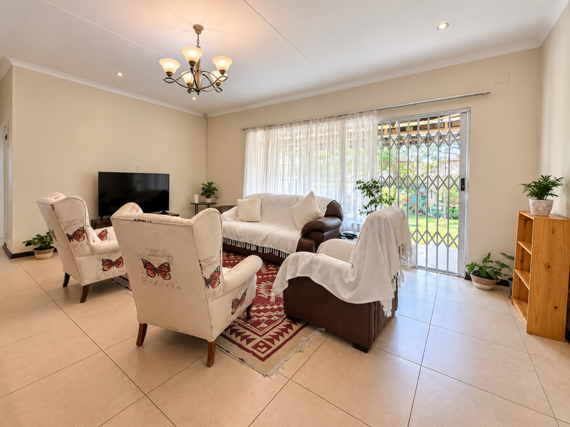 A bright and well-maintained living room featuring large format floor tiles, a sliding glass door with security gate, and elegant ceiling lighting.