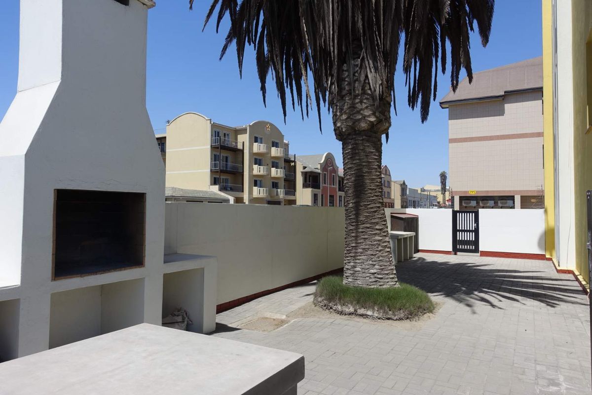 Outdoor courtyard area featuring a built-in masonry braai, paved flooring, and a mature palm tree within a secure apartment complex setting.