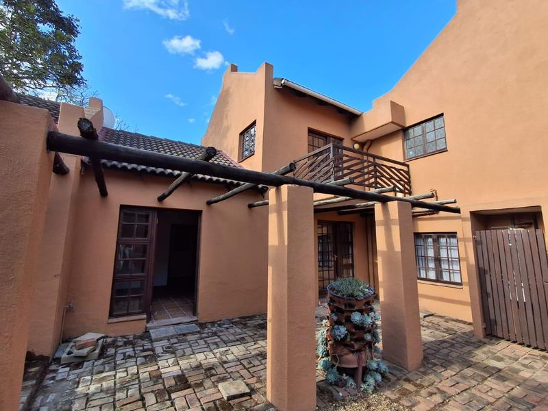 Rear exterior view of a cluster home featuring a brick-paved patio, a timber pergola, and an upper-level balcony with timber railings.