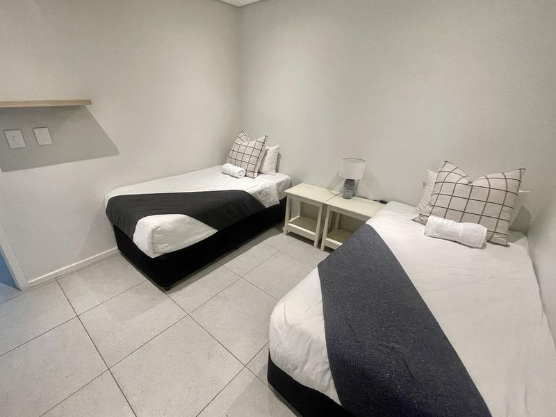 A clean and functional bedroom featuring neutral wall tones and large format floor tiles, providing a simple and comfortable living space.