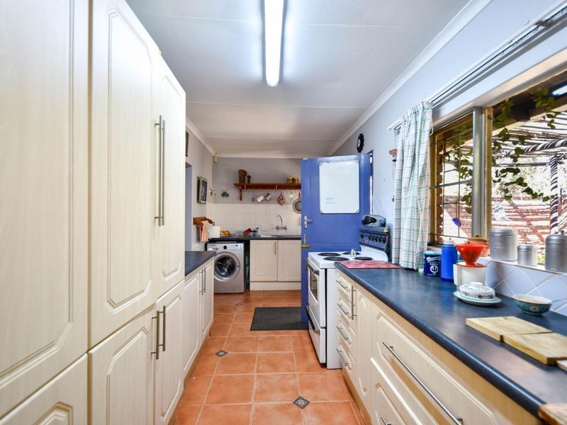 A functional galley-style kitchen featuring ample built-in cabinetry, laminate countertops, a freestanding stove, and tiled flooring with direct access to the exterior.