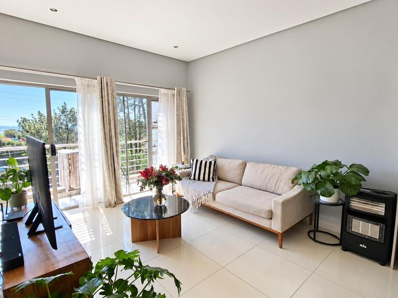 Bright and modern living room featuring large sliding glass doors that open to a balcony, complemented by neutral tiled flooring and recessed ceiling lighting.