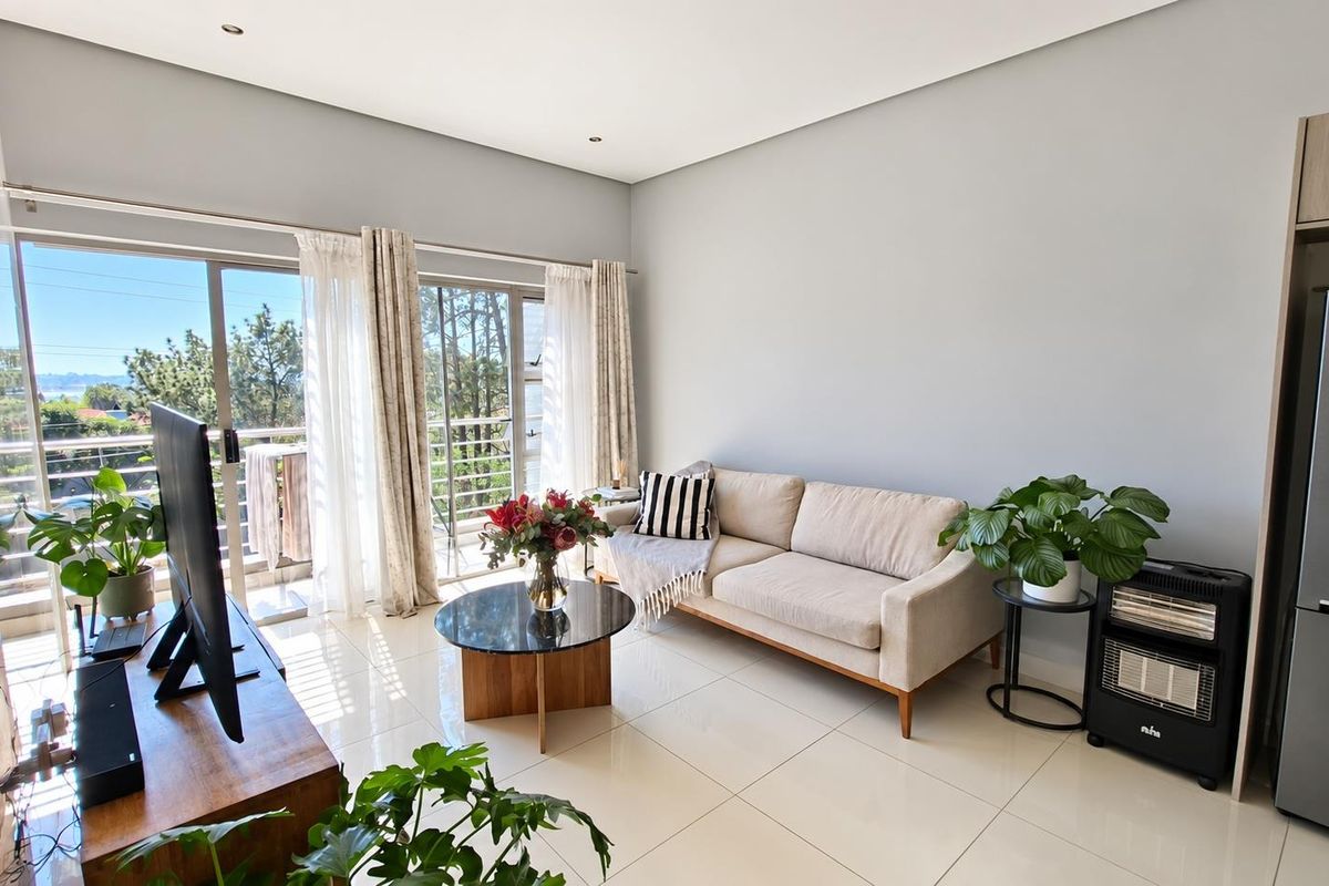 Bright and modern living room featuring large sliding glass doors that open to a balcony, complemented by neutral tiled flooring and recessed ceiling lighting.