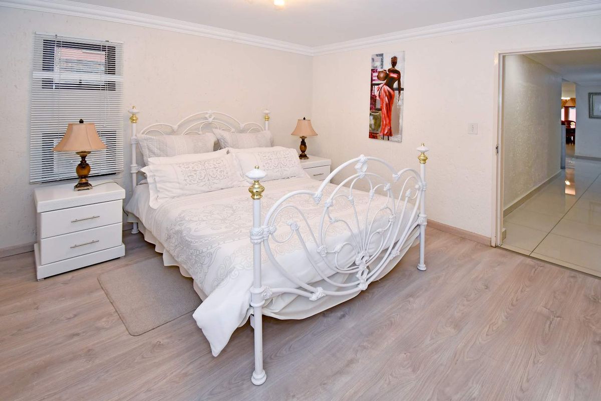 A well-maintained bedroom featuring light-toned laminate flooring, crown molding, and a window with fitted blinds.