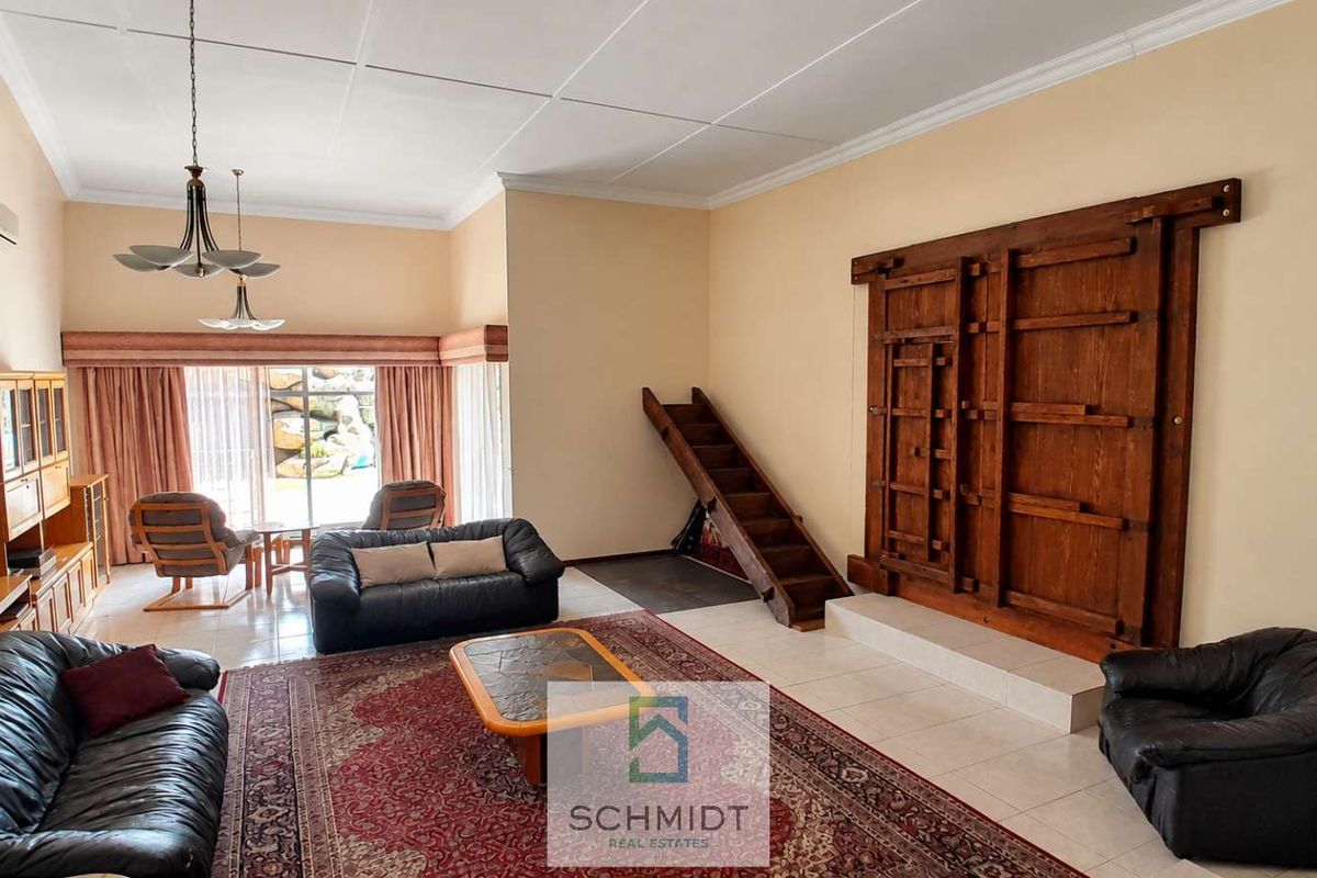 Spacious living room featuring tiled flooring, a decorative wooden wall panel, and a staircase leading to an upper level.