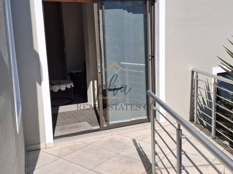 A clean, tiled balcony area featuring a modern stainless steel balustrade and a sliding glass door providing access to the interior.