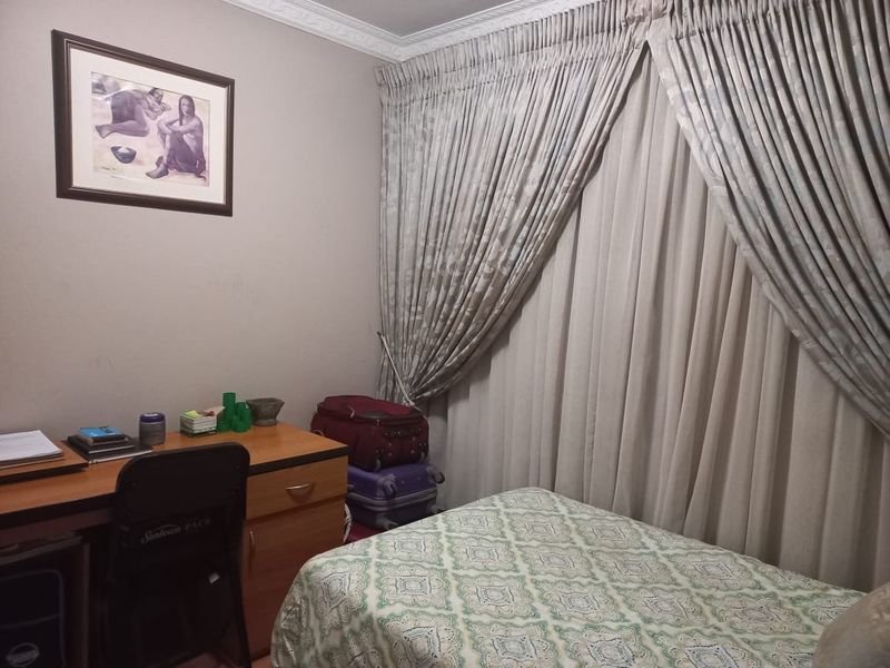 A functional bedroom featuring neutral wall tones, decorative ceiling cornicing, and full-length window curtains.