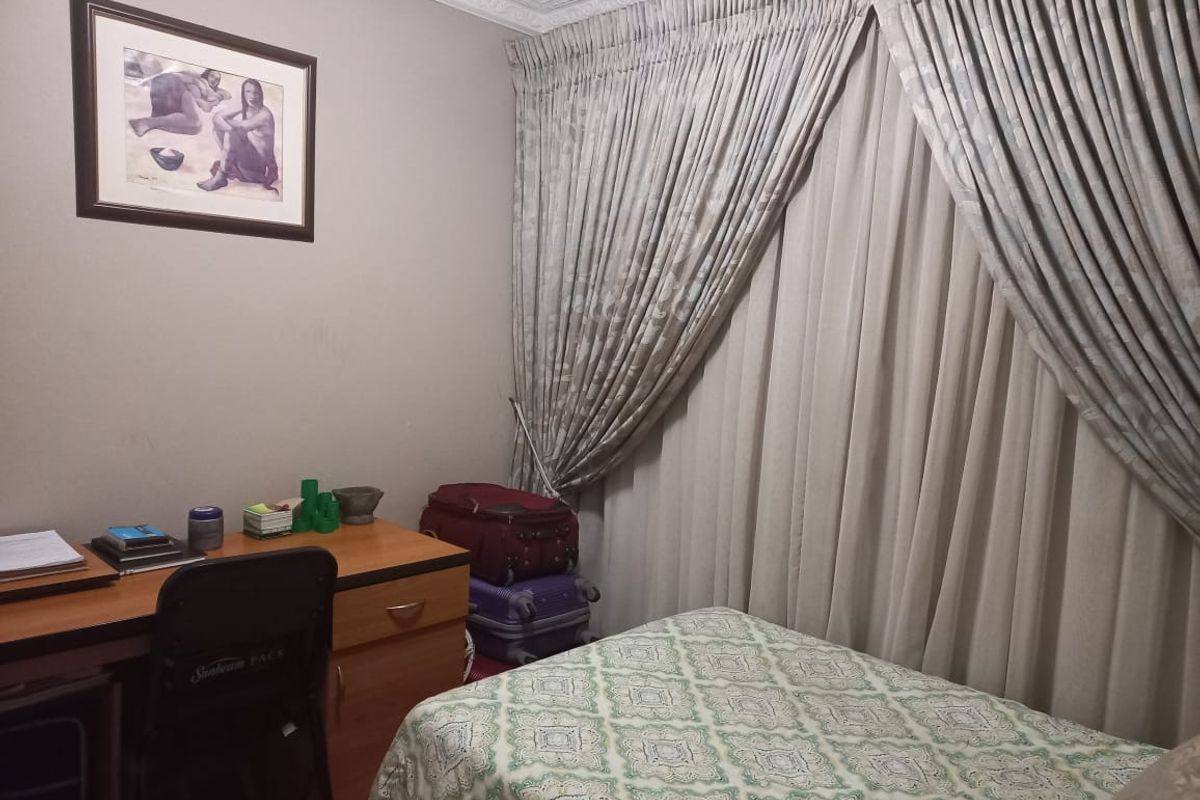 A functional bedroom featuring neutral wall tones, decorative ceiling cornicing, and full-length window curtains.