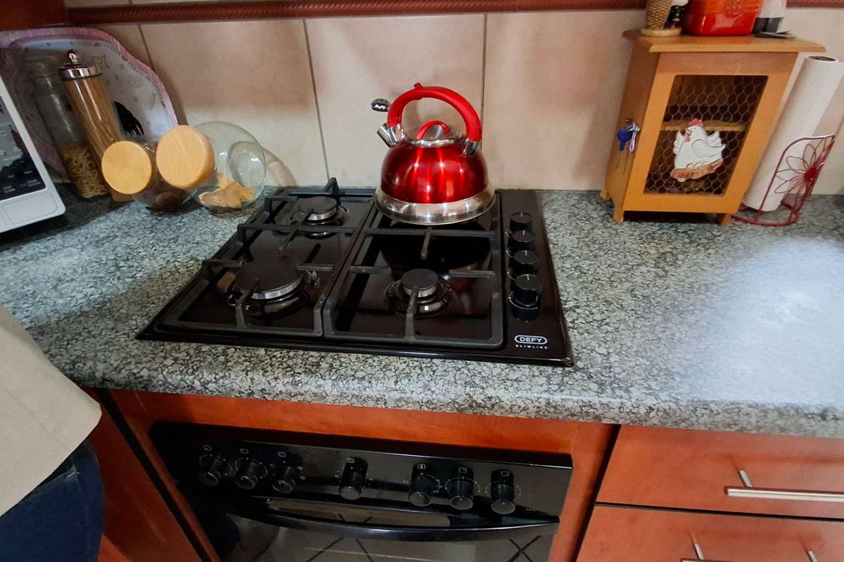 A functional kitchen area featuring a built-in gas hob, oven, granite countertops, and tiled backsplash with wooden cabinetry.