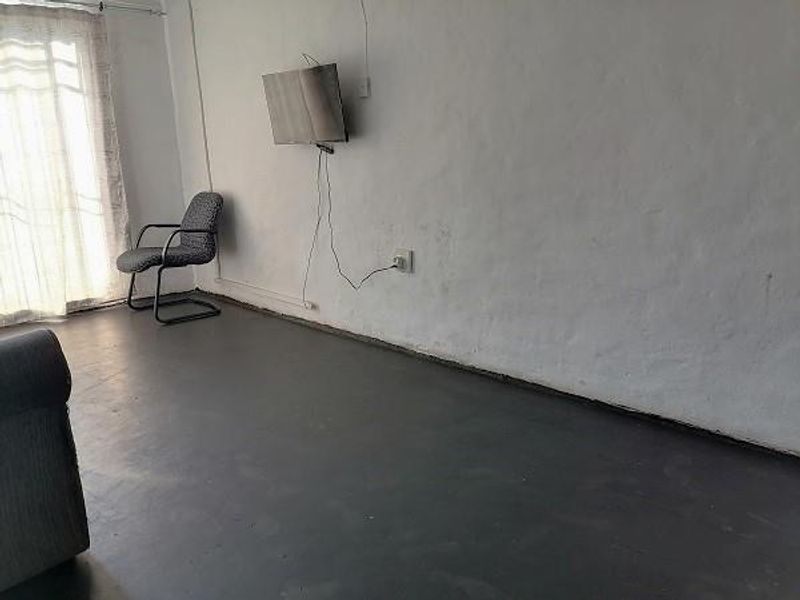 A living room area featuring painted concrete flooring and a sliding glass door, requiring cosmetic updates to the wall finishes and electrical management.