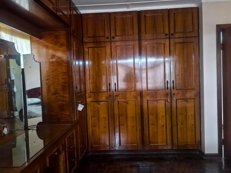 A bedroom featuring extensive built-in wooden cabinetry, a matching vanity unit, and traditional parquet flooring.