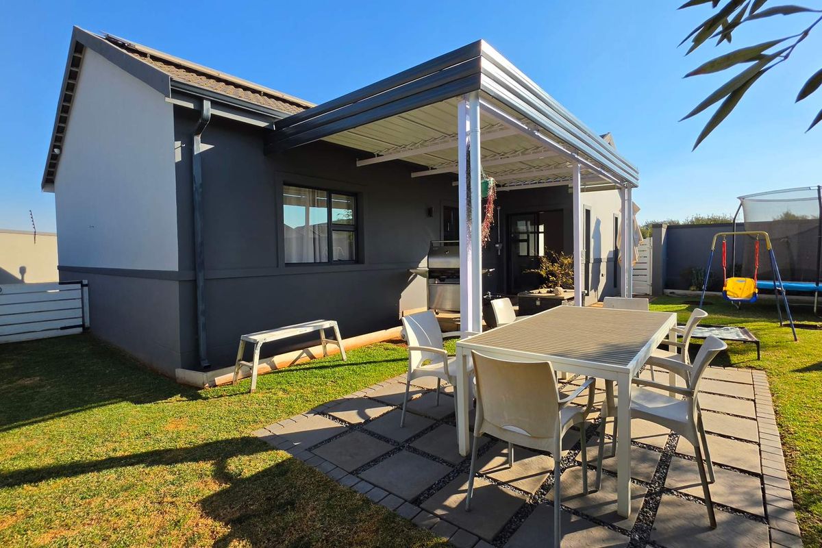 Rear exterior view of the property featuring a covered patio area with paved flooring and a well-maintained garden.
