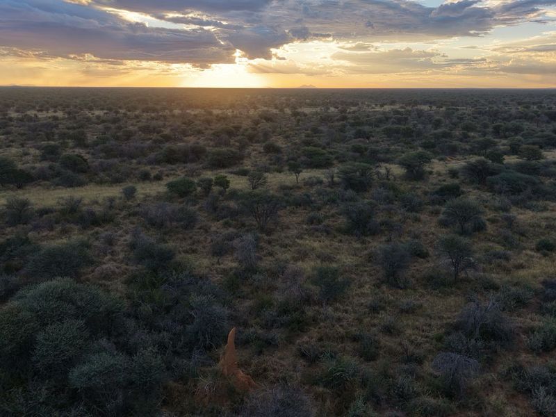 An expansive aerial view of the natural savannah landscape at sunset, showcasing the vast open terrain of the small holding.