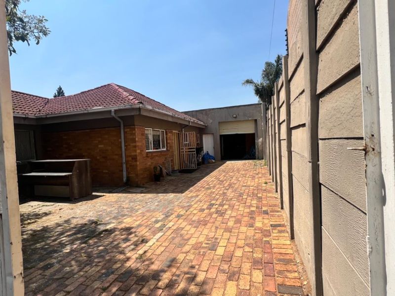 Rear exterior view showing a brick-paved driveway, precast boundary wall, and access to the garage and main dwelling structure.