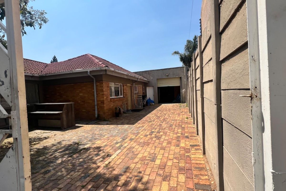 Rear exterior view showing a brick-paved driveway, precast boundary wall, and access to the garage and main dwelling structure.