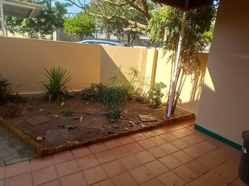 A covered patio area featuring tiled flooring and an adjacent small garden bed with a boundary wall, providing a private outdoor space.