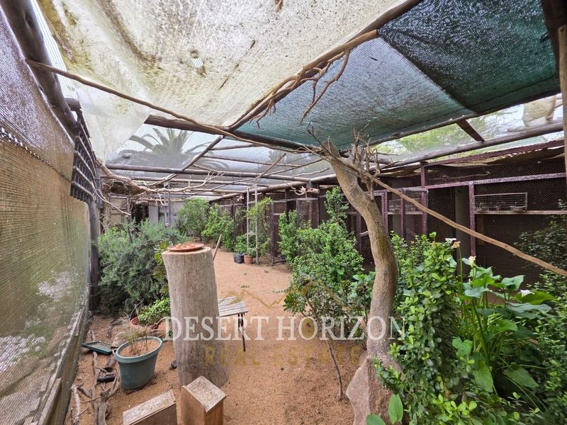 An outdoor utility enclosure featuring a mesh structure with shade cloth roofing and gravel flooring, suitable for animal housing or specialized storage.