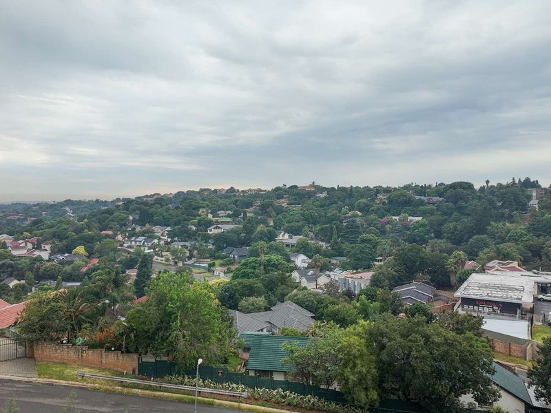 An elevated panoramic view overlooking a lush, tree-lined residential neighborhood under a cloudy sky.