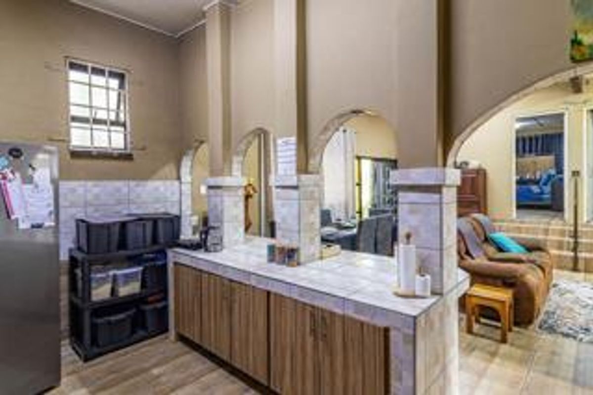 A kitchen area featuring tiled countertops, wooden cabinetry, and arched architectural details, opening into an adjacent living space.