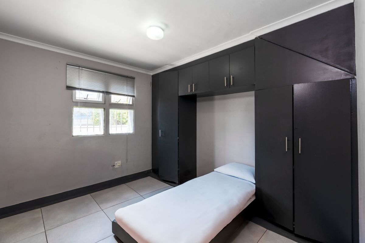 A bedroom featuring built-in dark cabinetry with overhead storage and tiled flooring, providing a functional and compact living space.