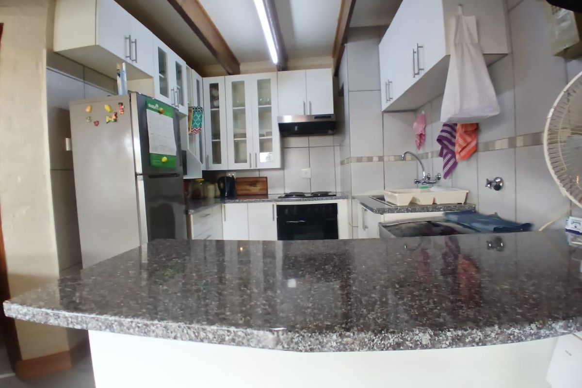 A functional kitchen featuring granite countertops, white cabinetry with glass-fronted upper units, a built-in oven, and an extractor fan.