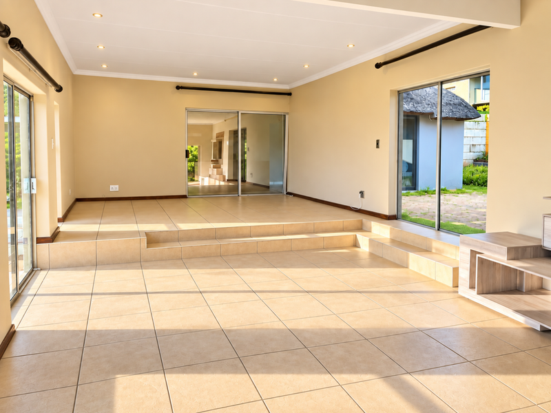 Spacious, sunlit living area featuring a sunken floor design, neutral tiled flooring, and multiple sliding glass doors providing seamless access to the garden.
