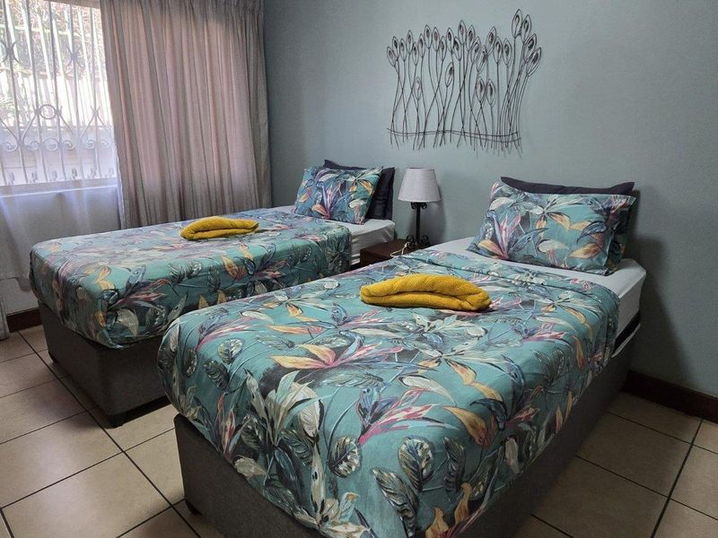 A functional bedroom featuring tiled flooring and a window fitted with security bars, providing a practical and well-lit sleeping space.