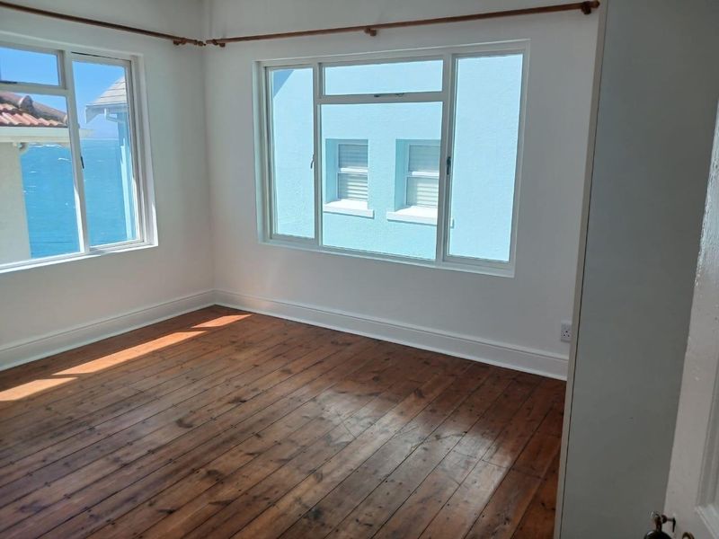 A bright, empty bedroom featuring original timber flooring, large windows with natural light, and neutral wall finishes.