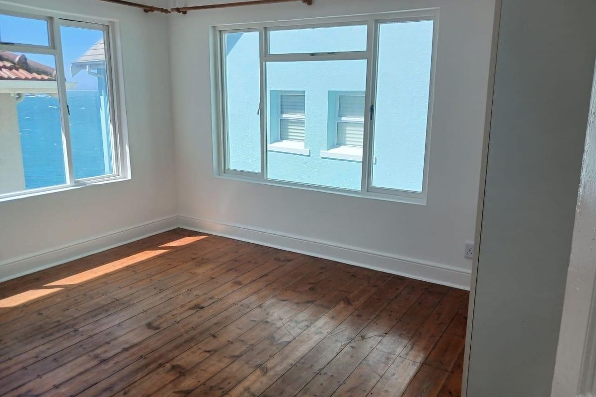 A bright, empty bedroom featuring original timber flooring, large windows with natural light, and neutral wall finishes.