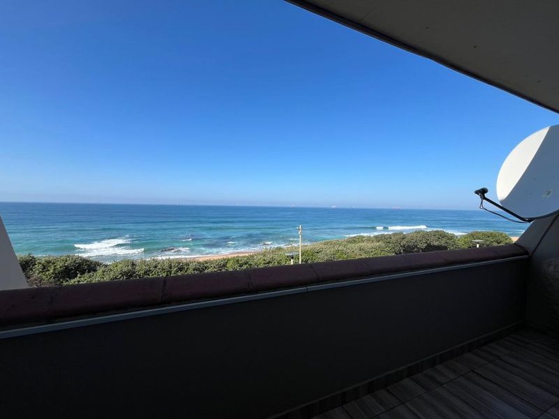 A spacious balcony featuring tiled flooring and a balustrade, offering expansive, unobstructed views of the ocean and coastline.