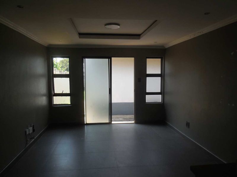 An empty living room featuring tiled flooring, a recessed ceiling with downlights, and a sliding glass door providing access to the exterior.