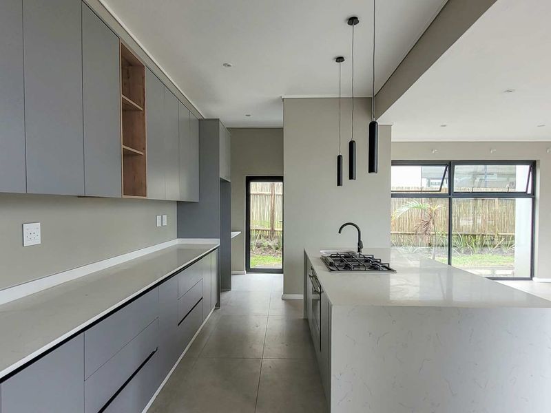 Modern open-plan kitchen featuring sleek grey cabinetry, stone countertops, a central island with a gas hob, and direct access to the outdoor area.