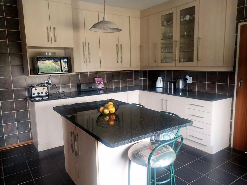 A functional kitchen featuring light-toned cabinetry, dark granite countertops, a central island, and dark tiled flooring with a matching backsplash.