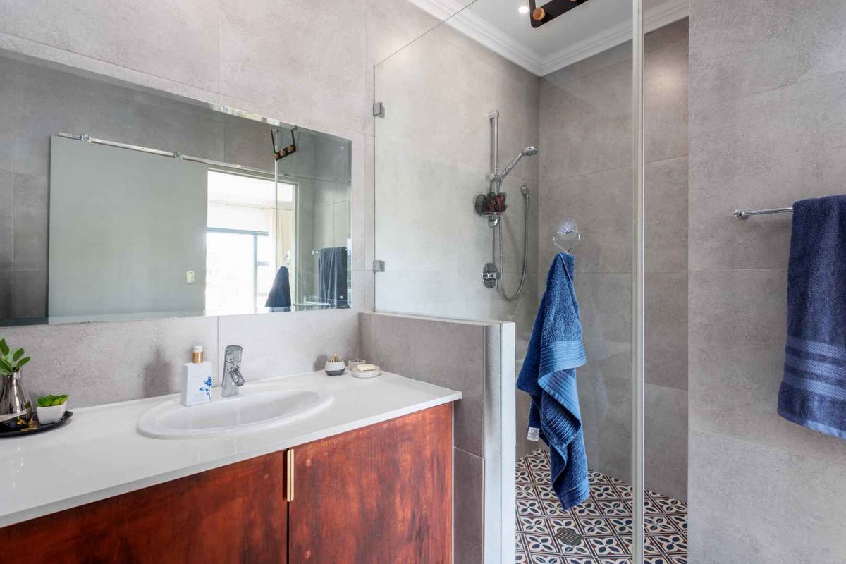 Modern bathroom featuring a vanity with a basin, a large wall mirror, and a walk-in shower with glass enclosure and patterned floor tiles.