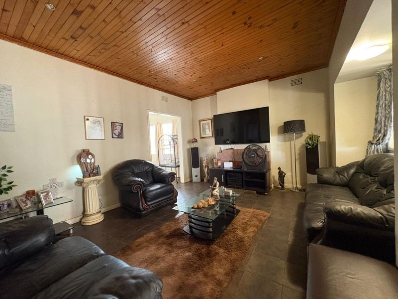 Spacious living room featuring dark tiled flooring and a warm timber tongue and groove ceiling with recessed lighting.