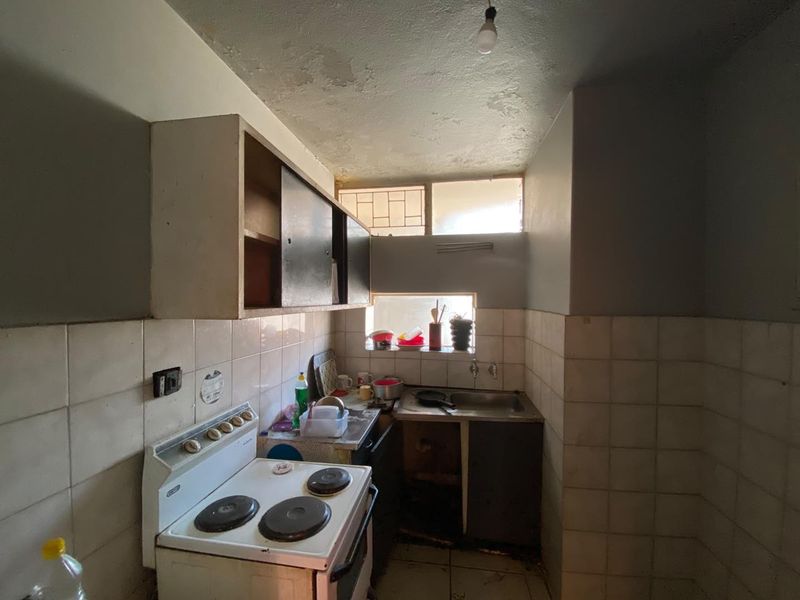 A compact, dated kitchen featuring a freestanding electric stove, tiled splashbacks, and original cabinetry in need of renovation and repair.