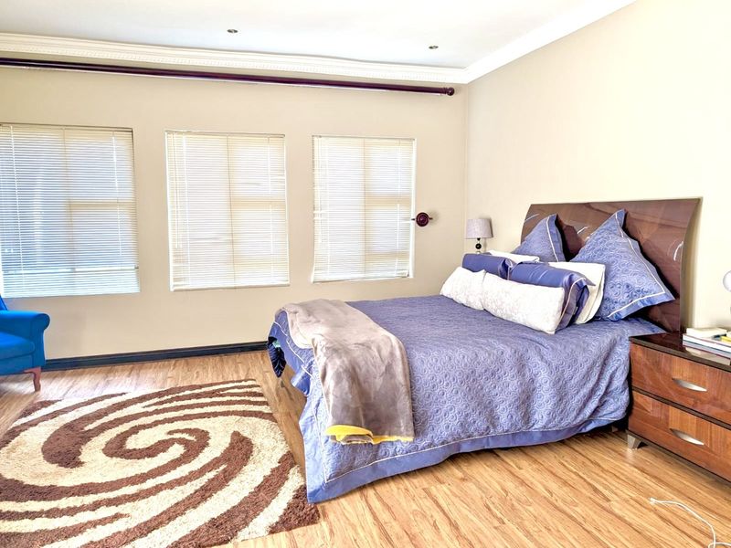A well-lit bedroom featuring laminate flooring, crown molding, and three windows fitted with venetian blinds.