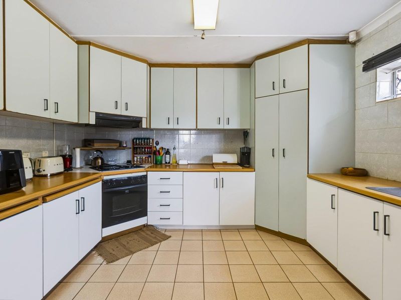 A functional kitchen featuring white built-in cabinetry, laminate countertops, a gas hob, and tiled flooring with a neutral backsplash.