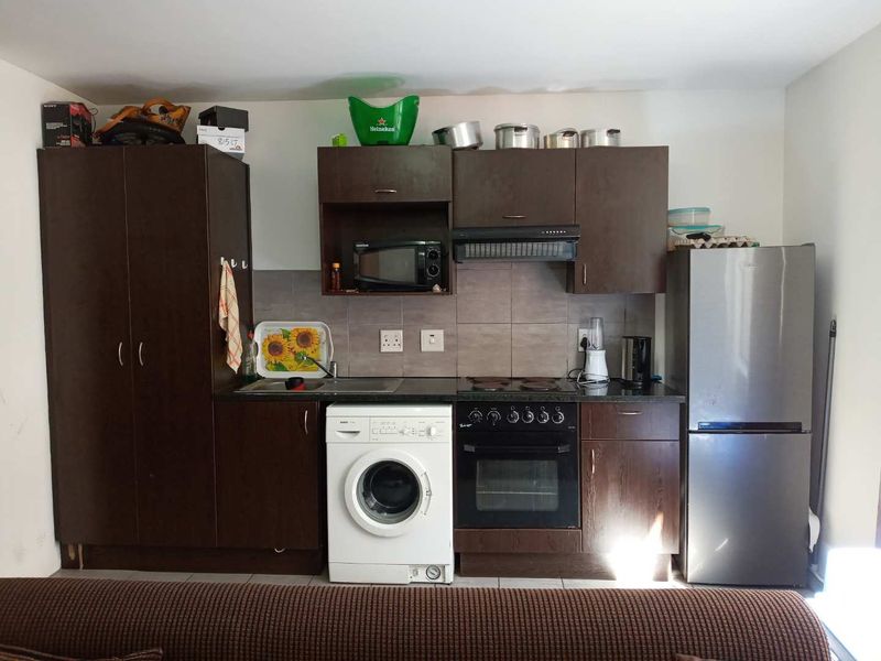 Compact kitchen featuring dark wood cabinetry, built-in oven, electric hob, extractor fan, and tiled backsplash with integrated sink and laundry appliance space.