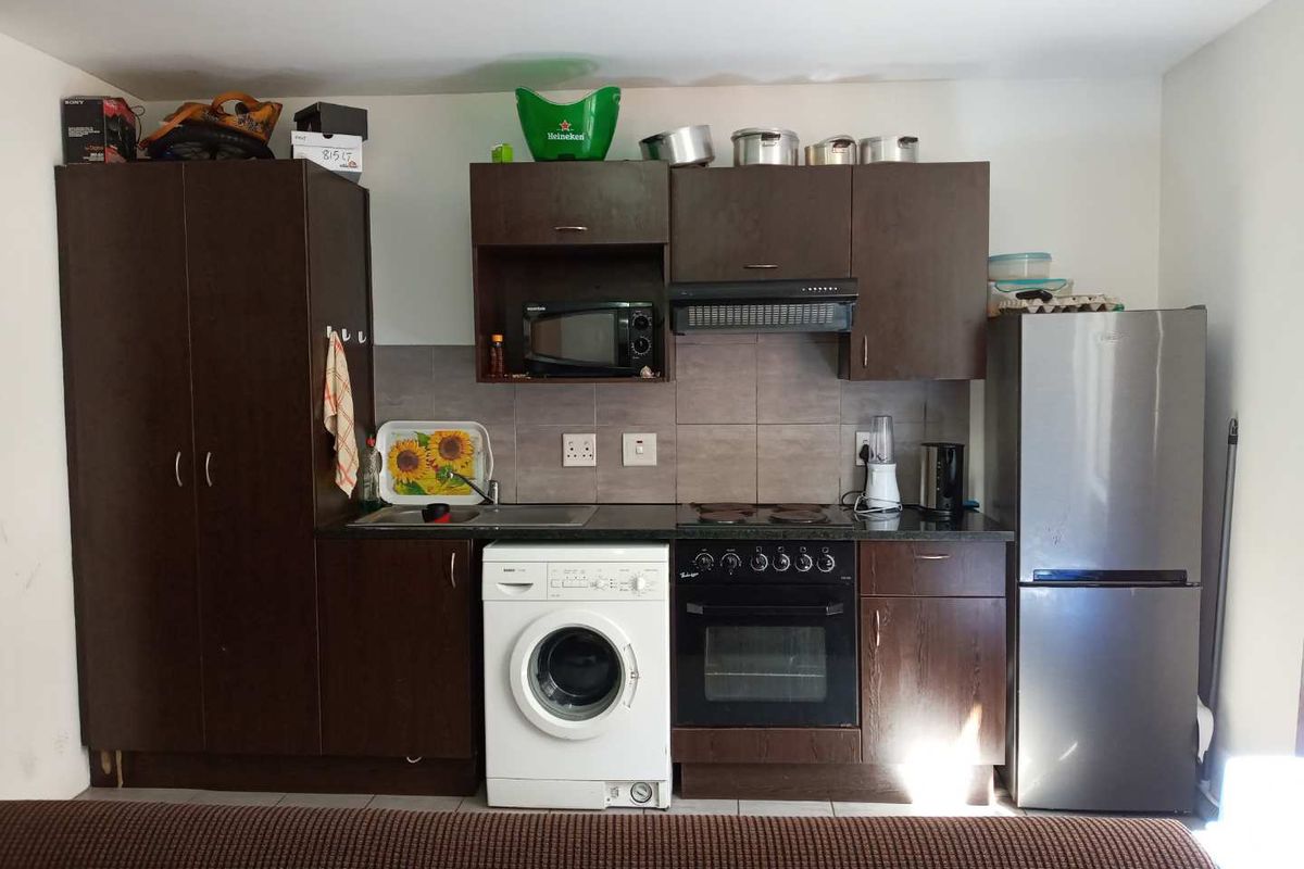 Compact kitchen featuring dark wood cabinetry, built-in oven, electric hob, extractor fan, and tiled backsplash with integrated sink and laundry appliance space.