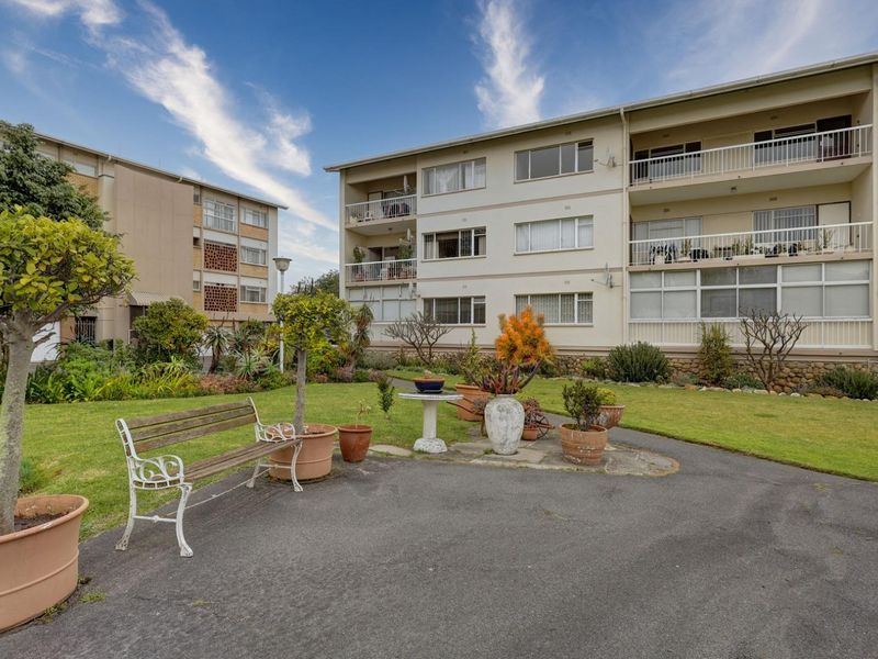 A view of the rear apartment building facade featuring multiple balconies, sliding windows, and a well-maintained communal garden area with paved pathways.