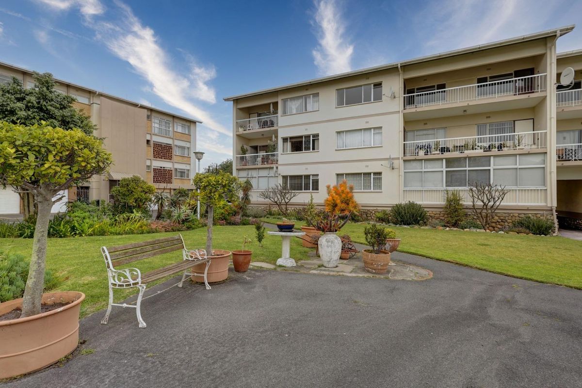 A view of the rear apartment building facade featuring multiple balconies, sliding windows, and a well-maintained communal garden area with paved pathways.