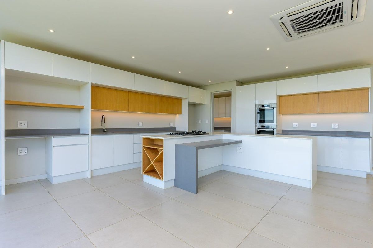 Modern, spacious kitchen featuring sleek white and wood-tone cabinetry, a central island with a cooktop, integrated appliances, and recessed lighting.
