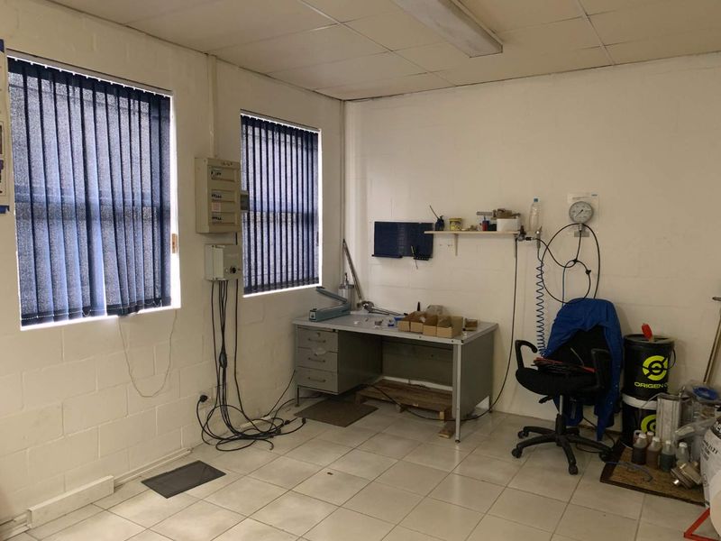 A functional utility or workshop space featuring tiled flooring, vertical blinds, and exposed blockwork walls, suitable for industrial or storage use.