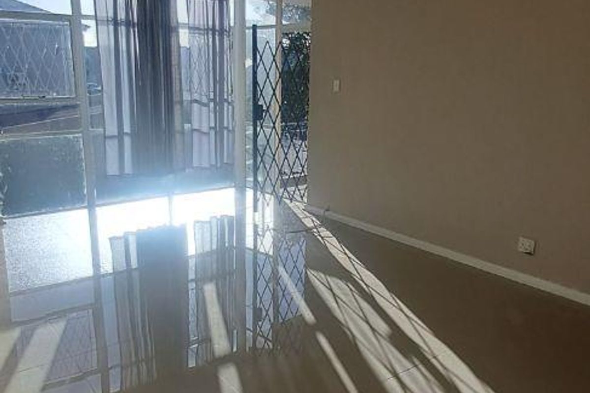 A bright, empty living room featuring tiled flooring, a ceiling light fixture, and a sliding glass door leading to an outdoor area with security gates.