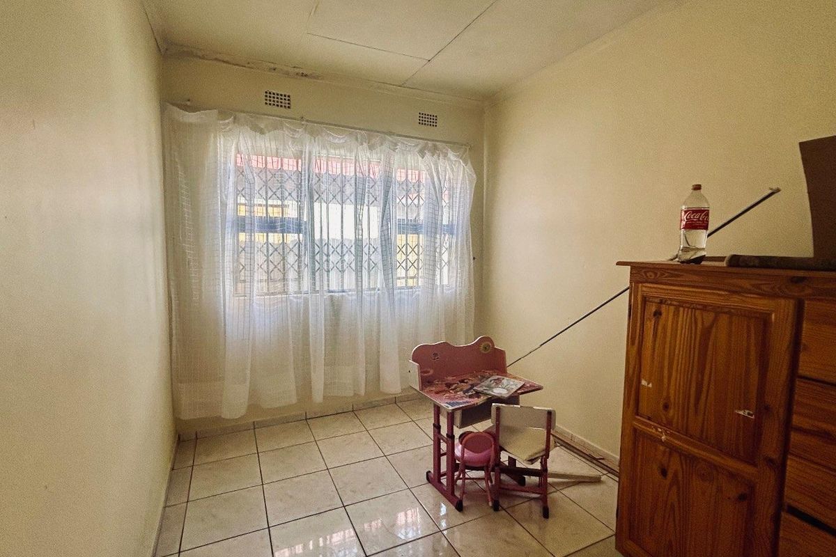 A compact bedroom featuring tiled flooring, a window with security bars, and basic ceiling finishes, offering a functional space for renovation.
